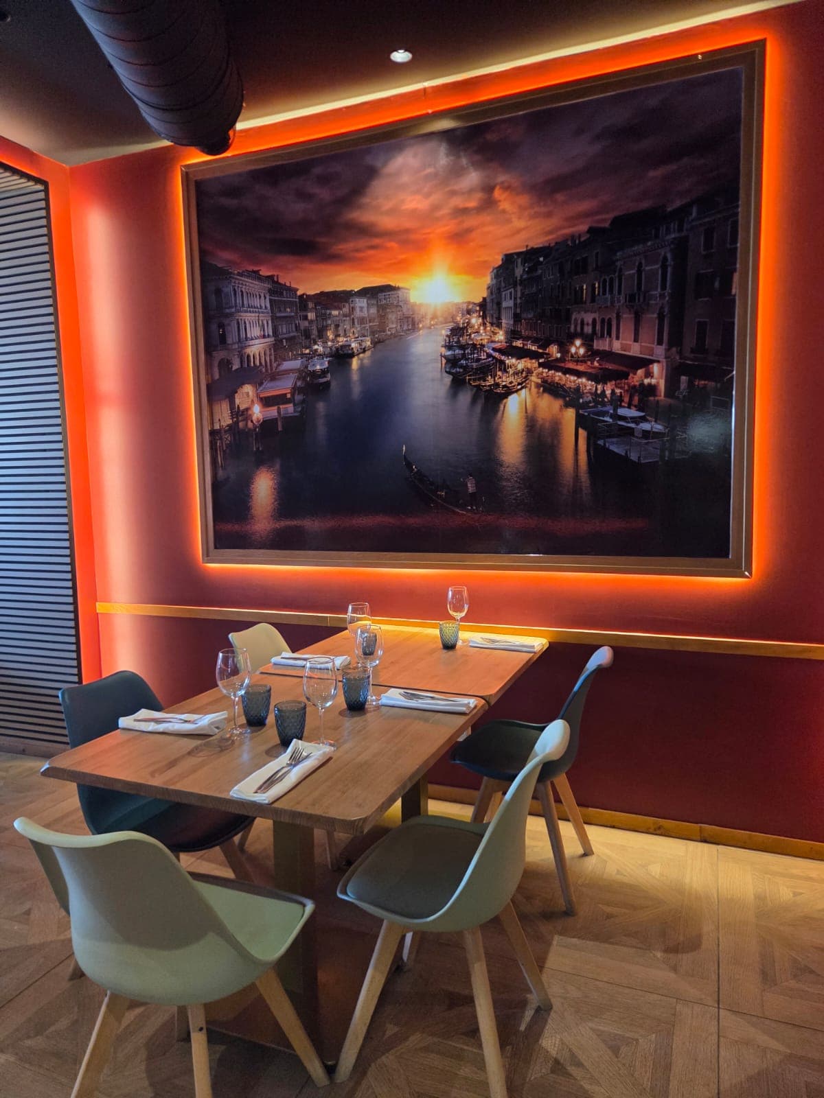 Mesa de restaurante preparada bajo un gran cuadro iluminado de un atardecer en Venecia.